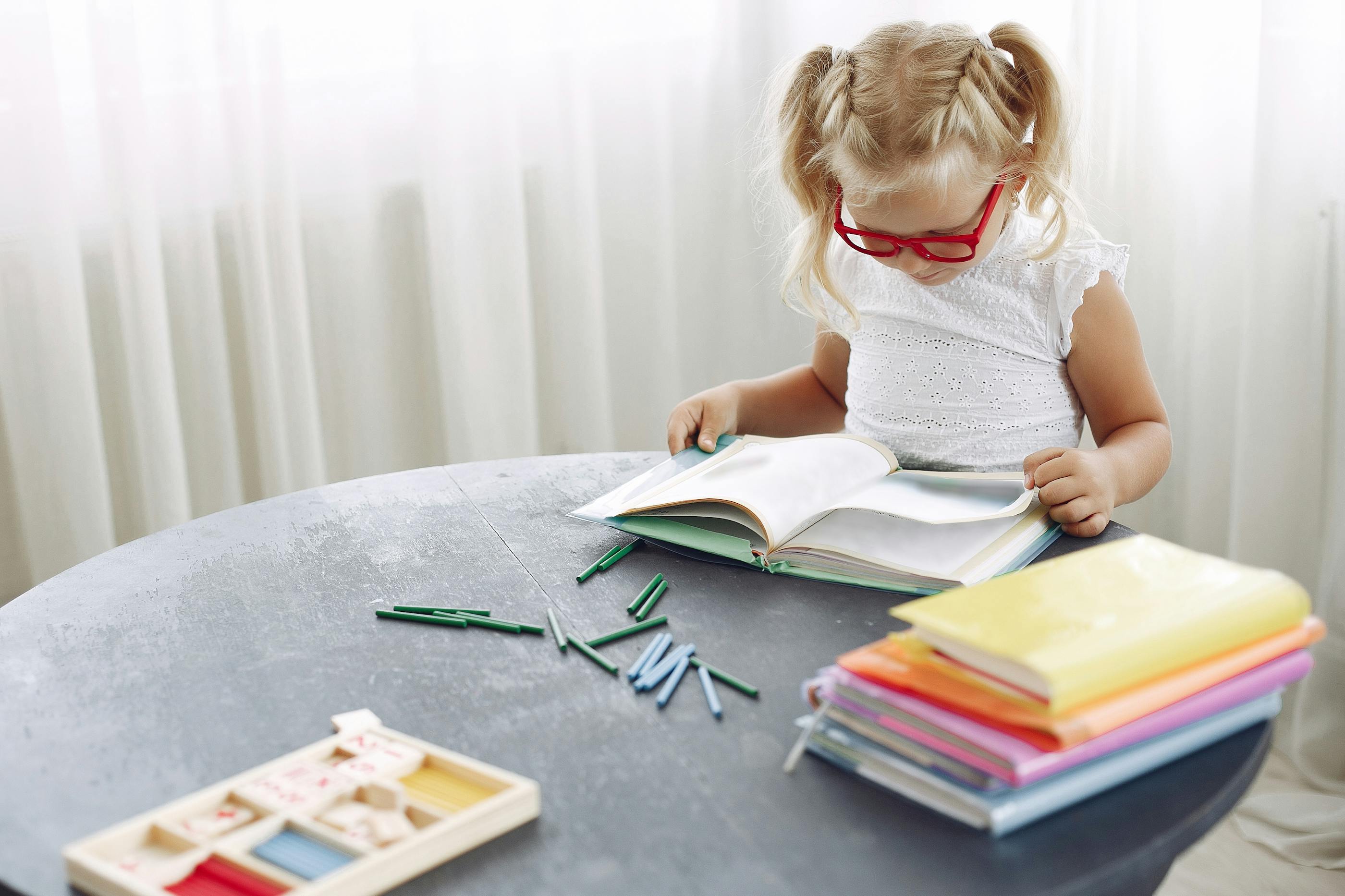 A young student reading a book at a table with letter tiles and colorful books