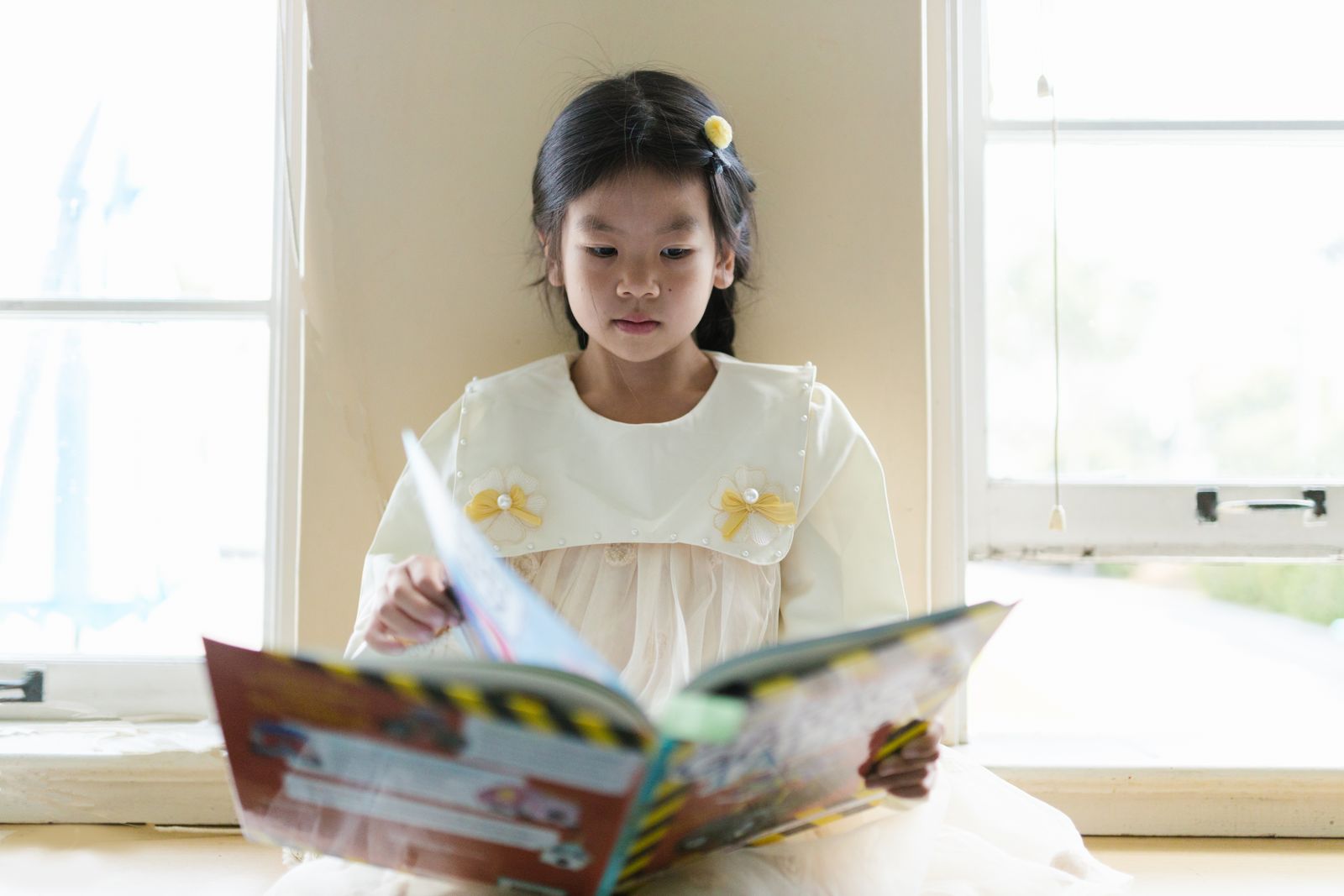 A child reading a picture book by a sunlit window